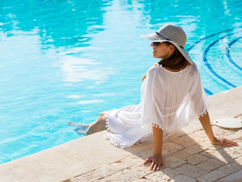 relaxed woman in white cover-up sitting at the edge of a commercial pool
